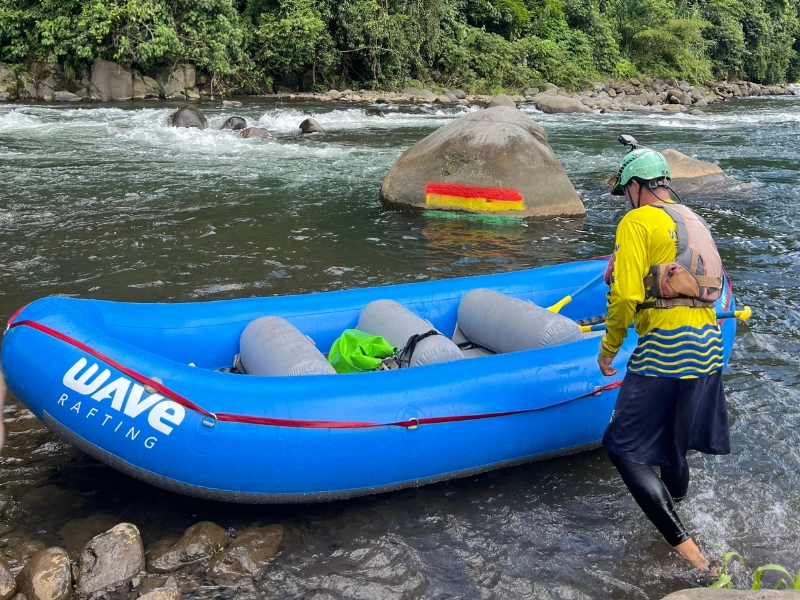 Rafting guide inspecting painted rock lines on the Sarapiquí River to check water levels before a white water tour.